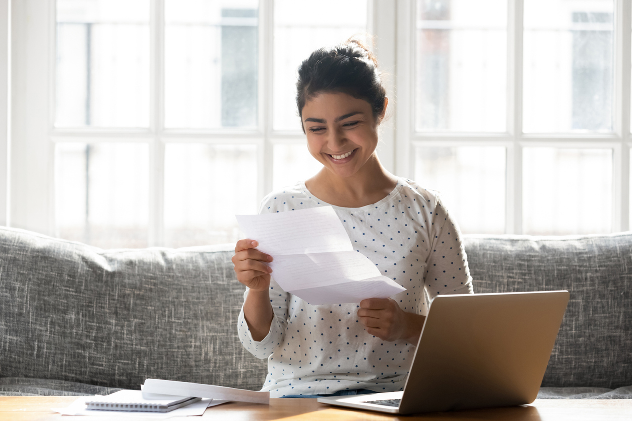 En kvinne som holder et ark og smiler foran et bord med en pc. Foto: Istockphoto.com