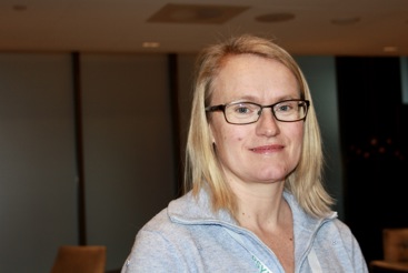 Kvinne med lyst hår og briller. Grå genser.