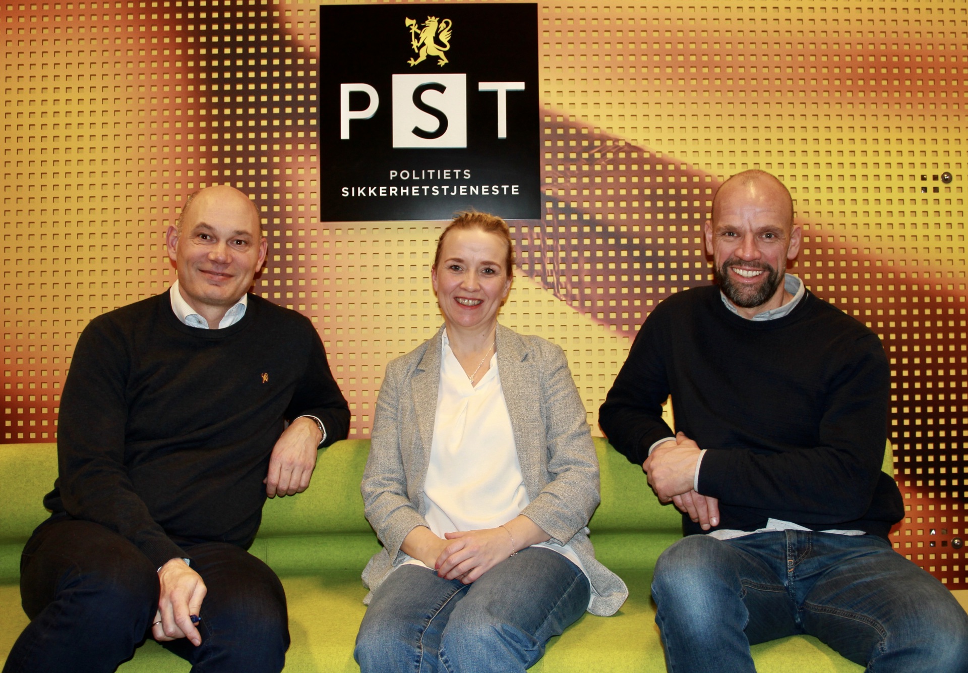 Tre personer i en grønn sofa foran gul bakgrunn med PST logo. I midten en kvinne med hvit bluse og grå blazer, på hver side men i mørk genser og bukse.