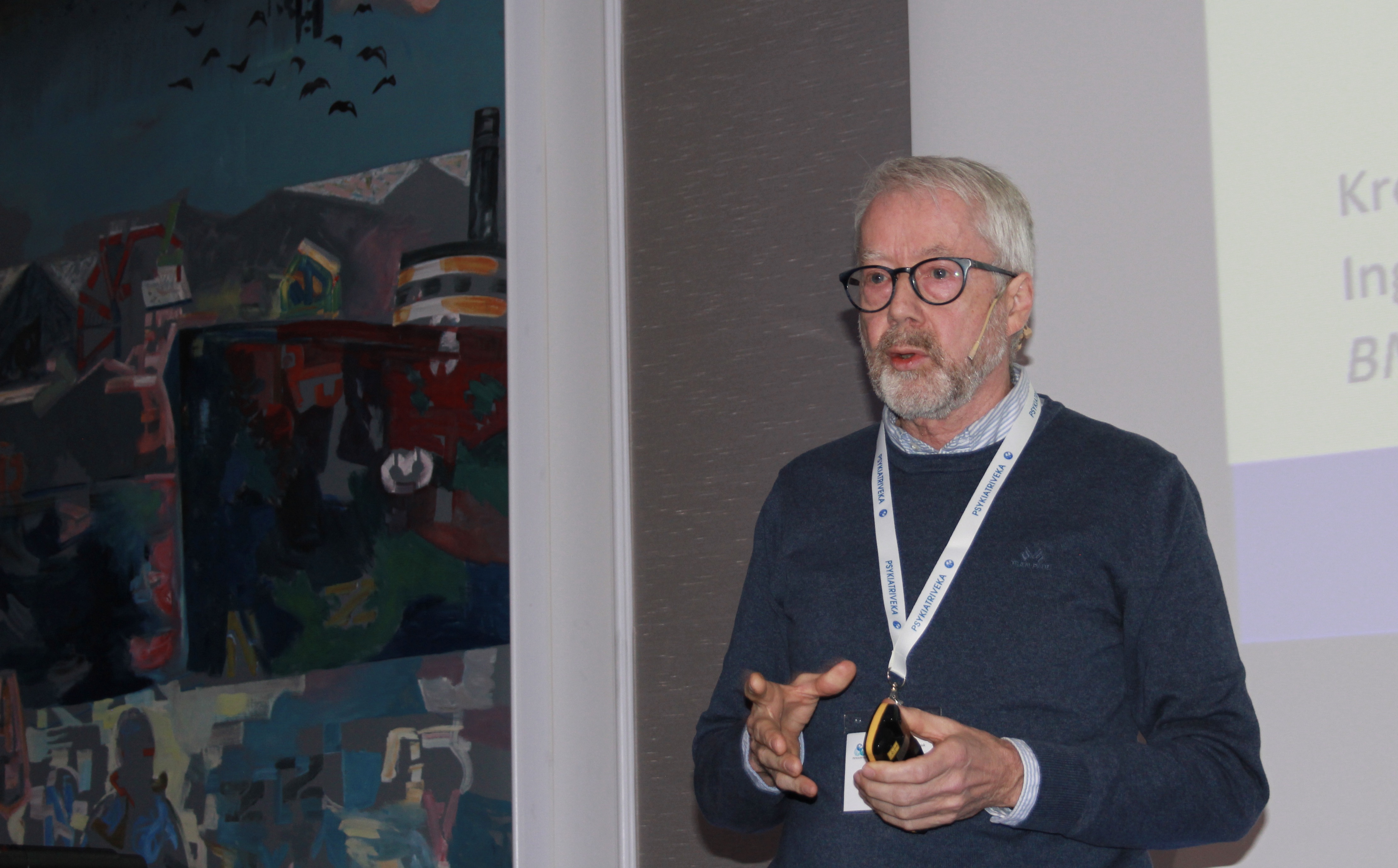 En mann i bl&aring; genser med gr&aring;tt h&aring;r og skjegg p&aring; et podium.