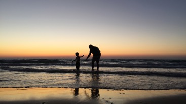 Pensjonist som leker med et barn i bølgene på stranden. Foto: Kron