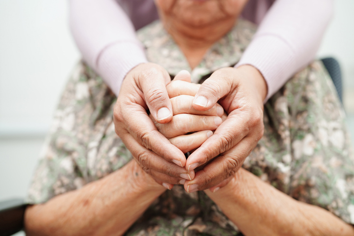 Bilde av helsepersonell som holder hendene til en eldre kvinne. Foto: manassanant pamai/iStock