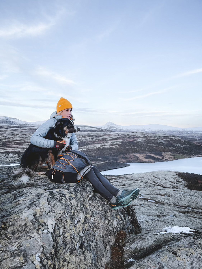 Bilde av Astrid Uhrenholdt Jacobsen som sitter på en sten sammen med hunden sin i vakre omgivelser.