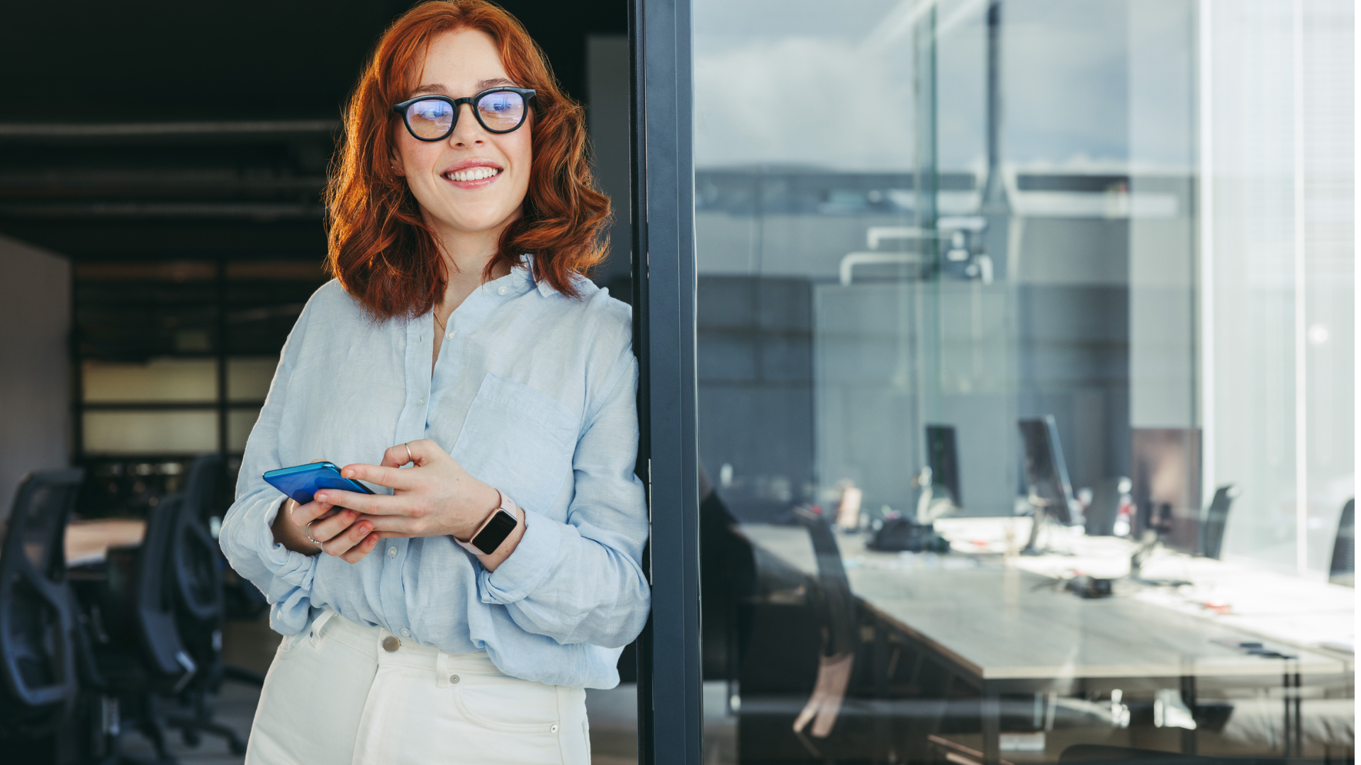 Dame med mobiltelefon i hendene som lener seg mot en døråpning. Foto: Akademikerne pluss