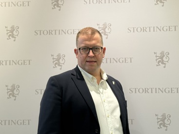 Leder for Allmenlegeforeningen, Hans-Christian Myklestul foran stortingets-logovegg. Han har kortklippet, lyst hår, firkantede briller med sort innfatning, har på seg sort dressjakke og hvit skjorte.