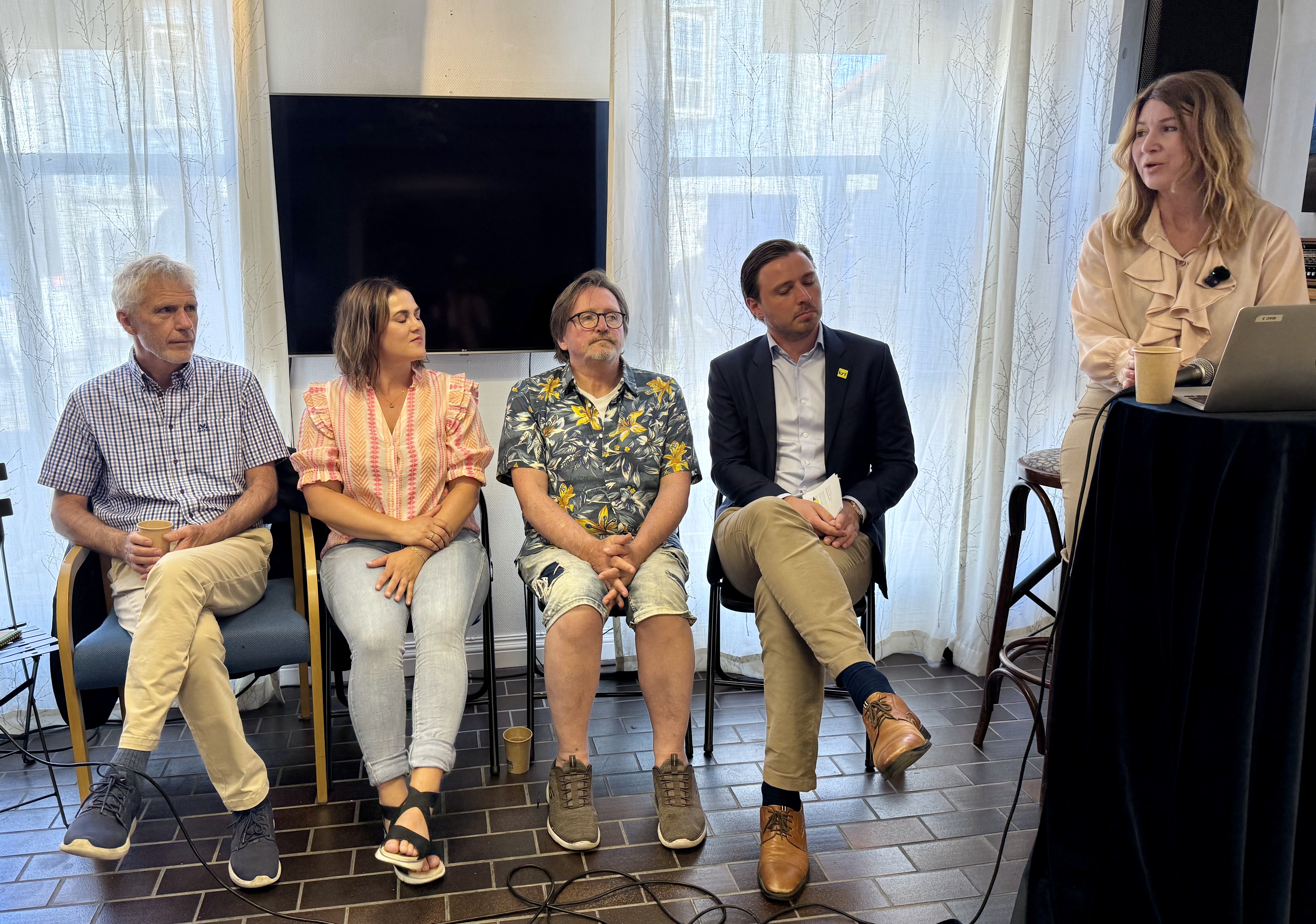 Fore mennesker sittende i hver sin stol. Panelsamtale. m&oslash;teleder ved talerstol.