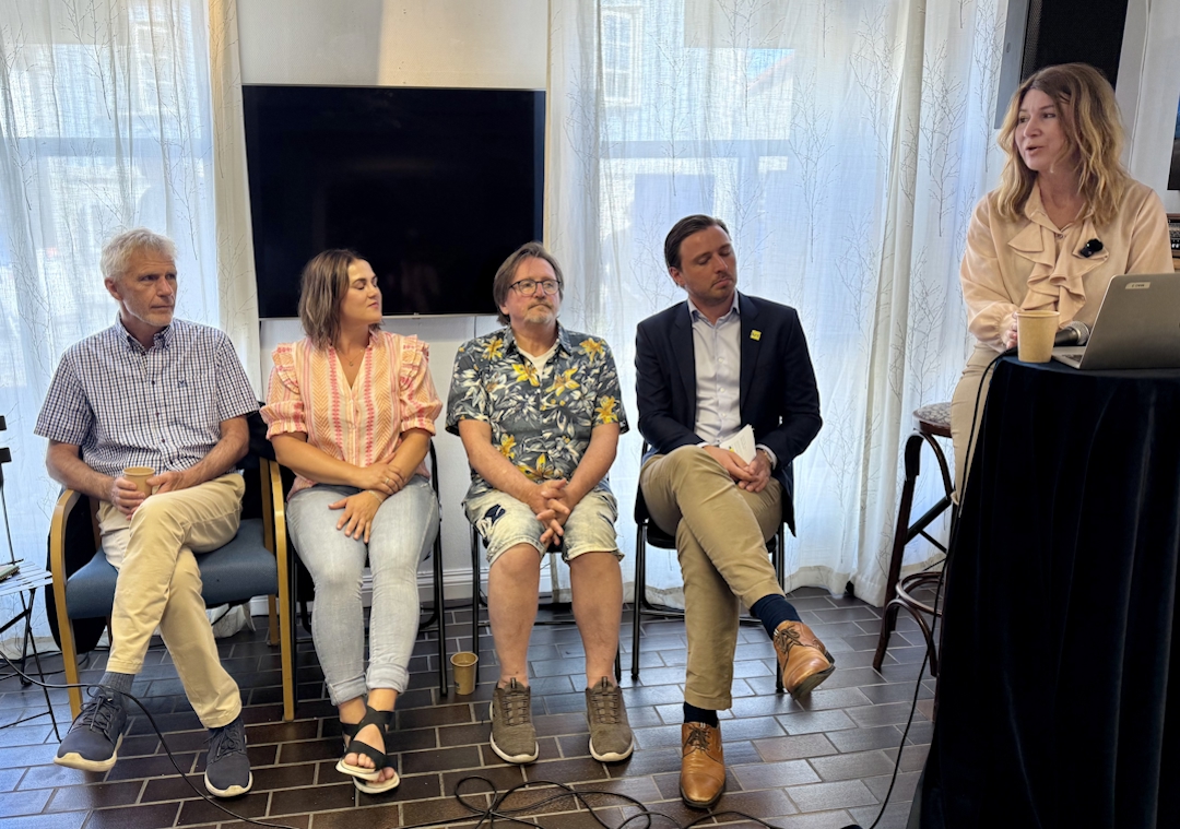 Fore mennesker sittende i hver sin stol. Panelsamtale. møteleder ved talerstol.