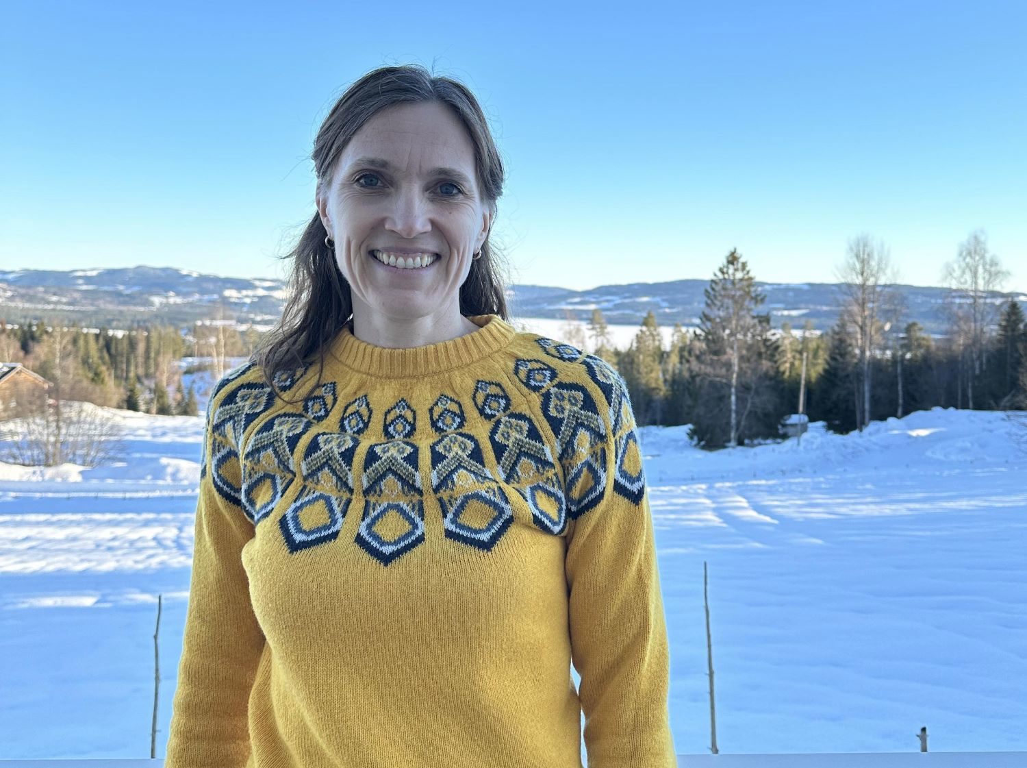 Bilde av Torhild Torjussen utendørs på gården i en gul ullgenser og stort smil. Foto: Privat