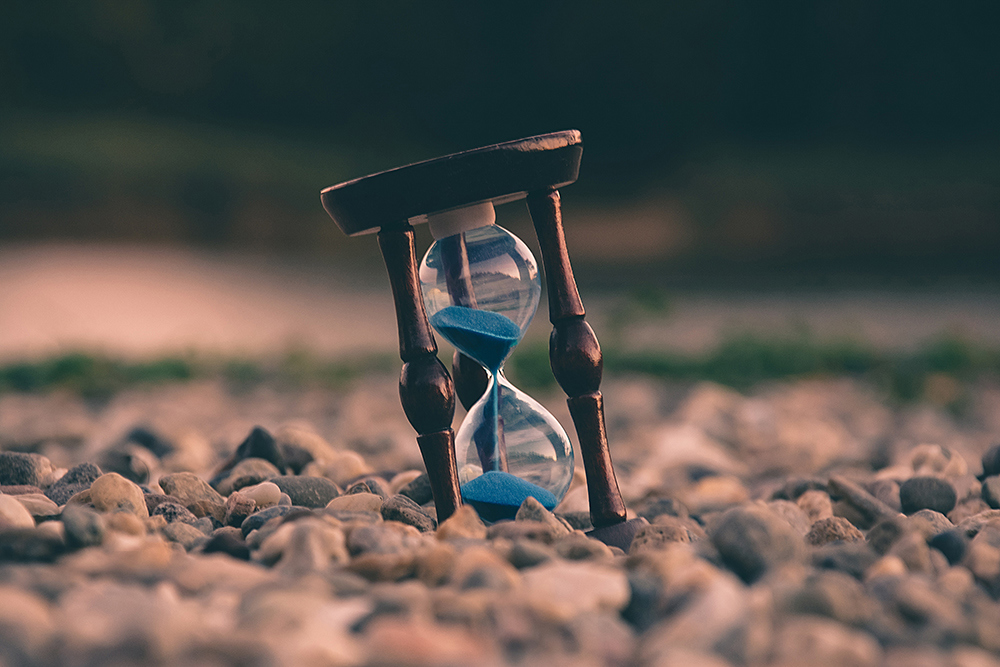 Aron Visuals, Unsplash. Bilde av et timeglass som står på et underlag av pukk og stein.