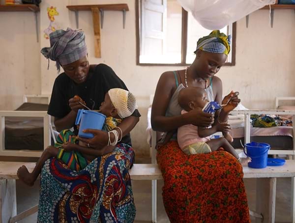 To kvinner gir barna mat i Sierra Leone