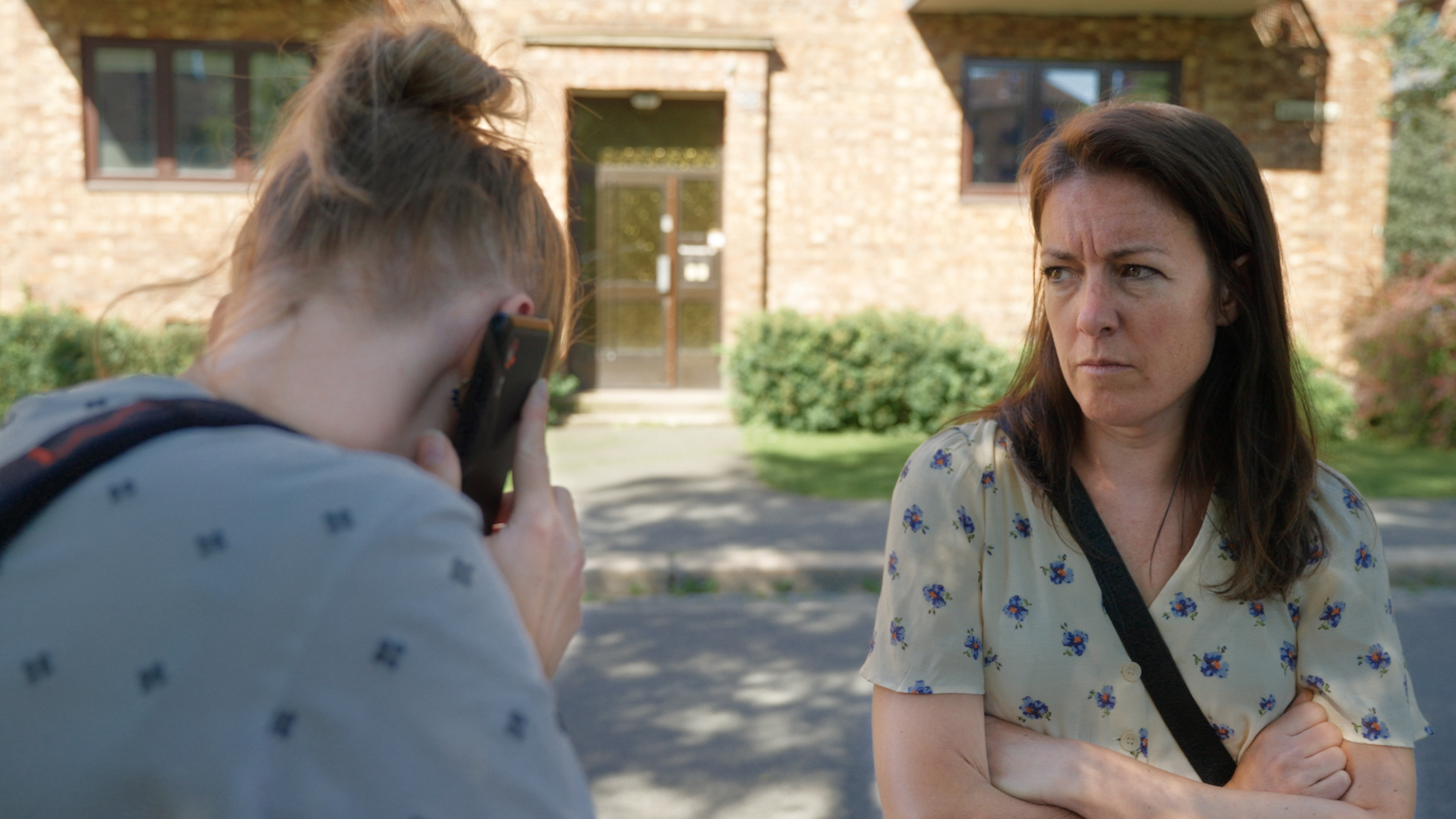 To kvinner ute p&aring; gata. r&oslash;d bygning bak. gr&oslash;nt gress.