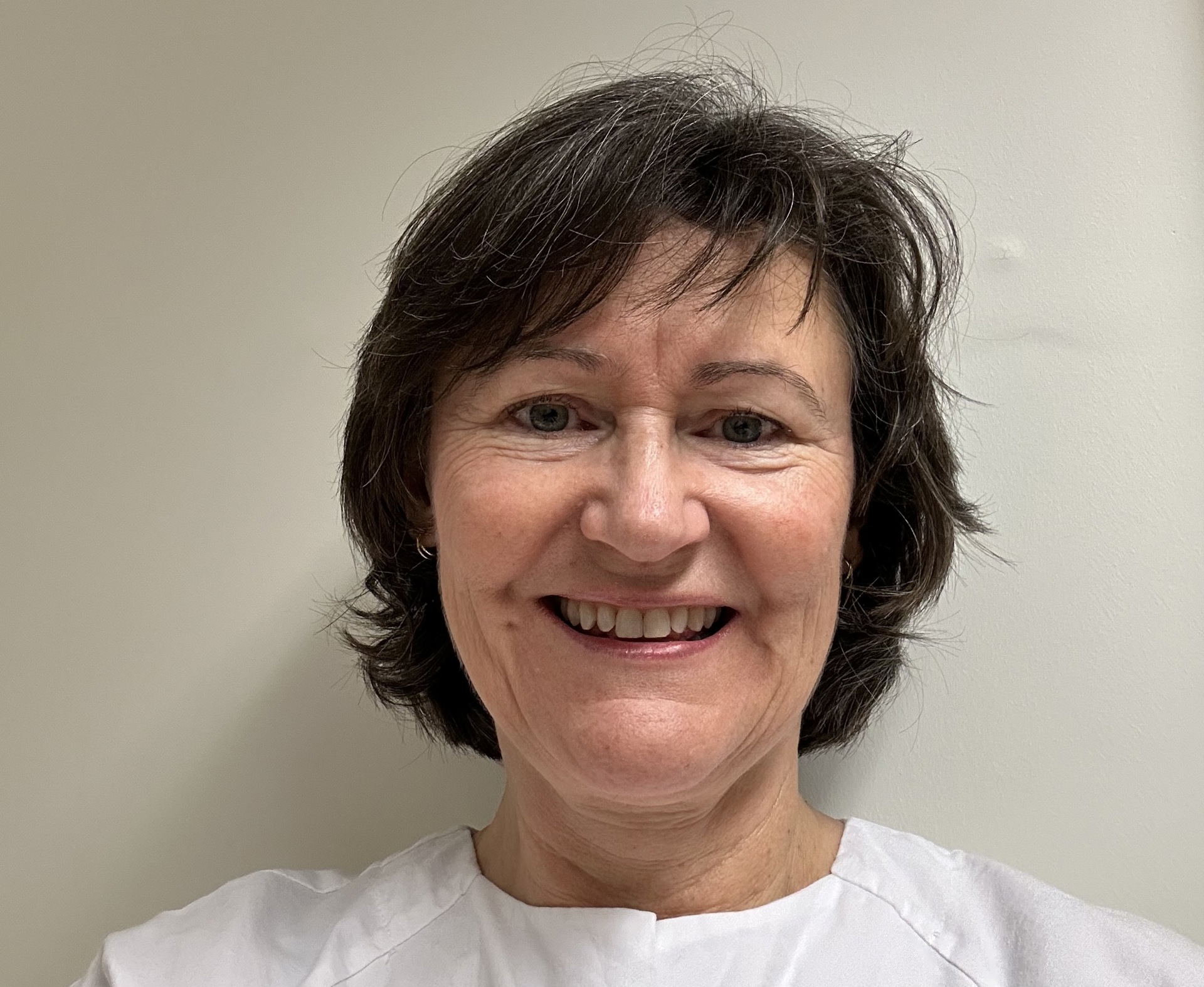 Kvinne, smilende, mørkt, kort hår, klinikktøy, nøytral bakgrunn