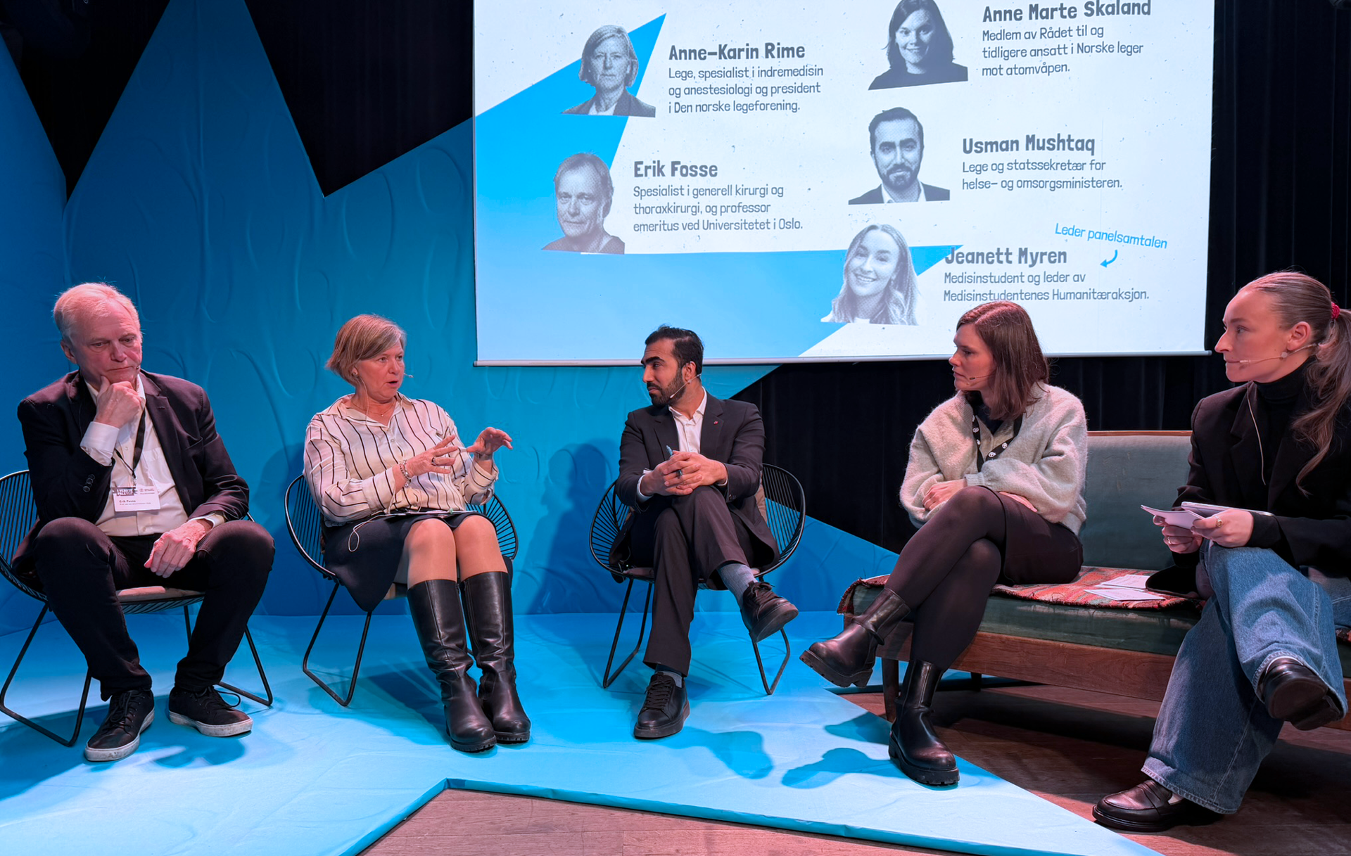 Fem mennesker sitter foran en blå bakgrunn formet som en skeiv stjerne. Fra venstre sitter Erik Fosse. Han har hvitt hår, hvit skjorte og mørk dress. Ved siden av ham sitter Anne-Karin Rime. Hun prater og er midt i gestikulasjon. Hun har lyst hår til rett nedforbi ørene, stripete skjorte, grått skjørt til knærne og høyre, sorte støvletter. Til høyre for Rime sitter Usman Mushtaq. Han sort hår og skjegg, hvit skjorte og grå dress. Ved siden av ham sitter Anne Marte Skaland. Hun har halvlangt, lysebrunt hår, lys strikkegenser og sorte bukser. Helt til høyre sitter  Jeanett Myren. Hun har lysebrunt hår i hestehale, sort pologenser og dressjakke, blå, løse jeans og mørke sko.   