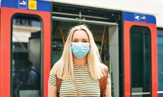 Dame med munnbind foran en åpen bussdør. Illustrasjonsfoto: Colourbox