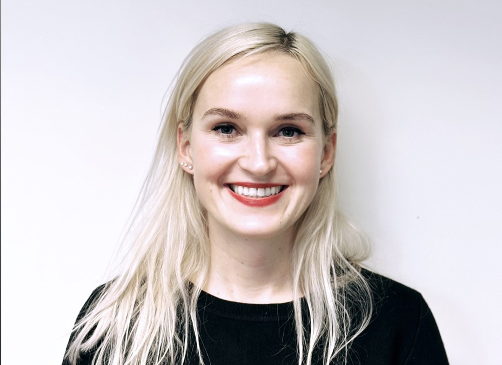 Smilende kvinne. Røde lepper. Langt lyst hår. Svart genser. Nøytral bakgrunn.