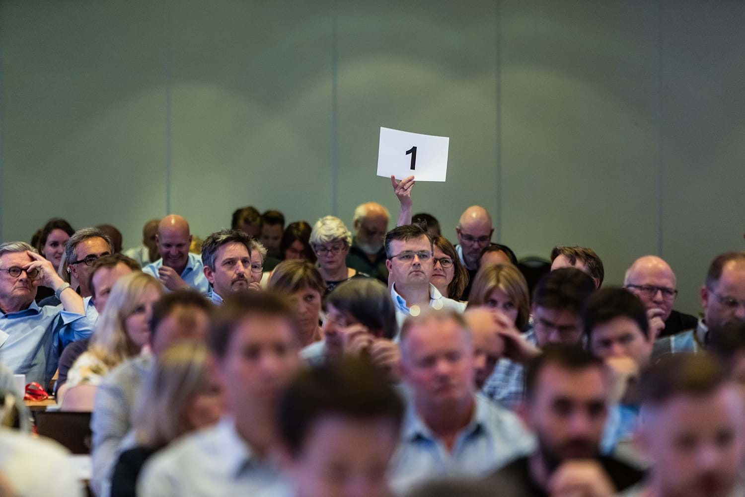 En person holder opp en lapp med et ettall i en sal med mennesker. Foto: Thomas Eckhoff/Legeforeningen