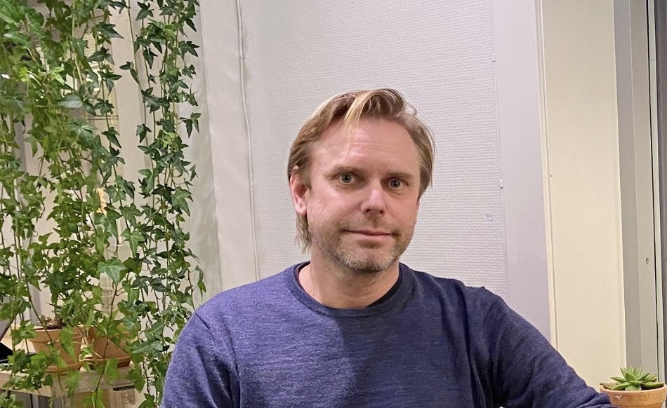 Mann, kort hår, blå genser. utendørs, hvit mur, grønne planter