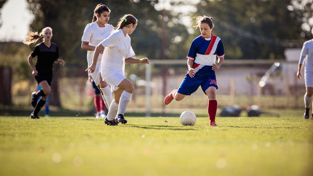 Unge, kvinnelige fotballspillere på en gresslette. Foto: skynesher.