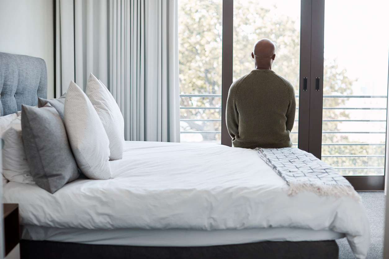 En eldre herre som sitter på hjørnet av en seng og ser ut vinduet. Foto: Istockphoto.com