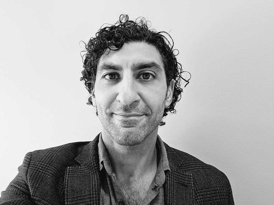 Mann med mørkt hår og mørk skjorte. Bildet er i sort hvitt.