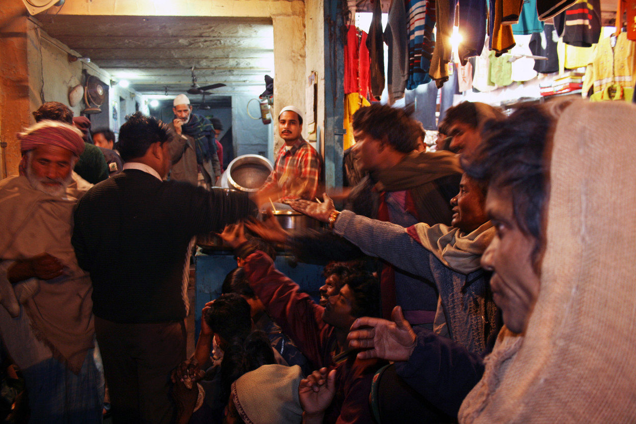 Mange mennesker, tett sammen, med utstrakte hender. Rekker seg etter mat.