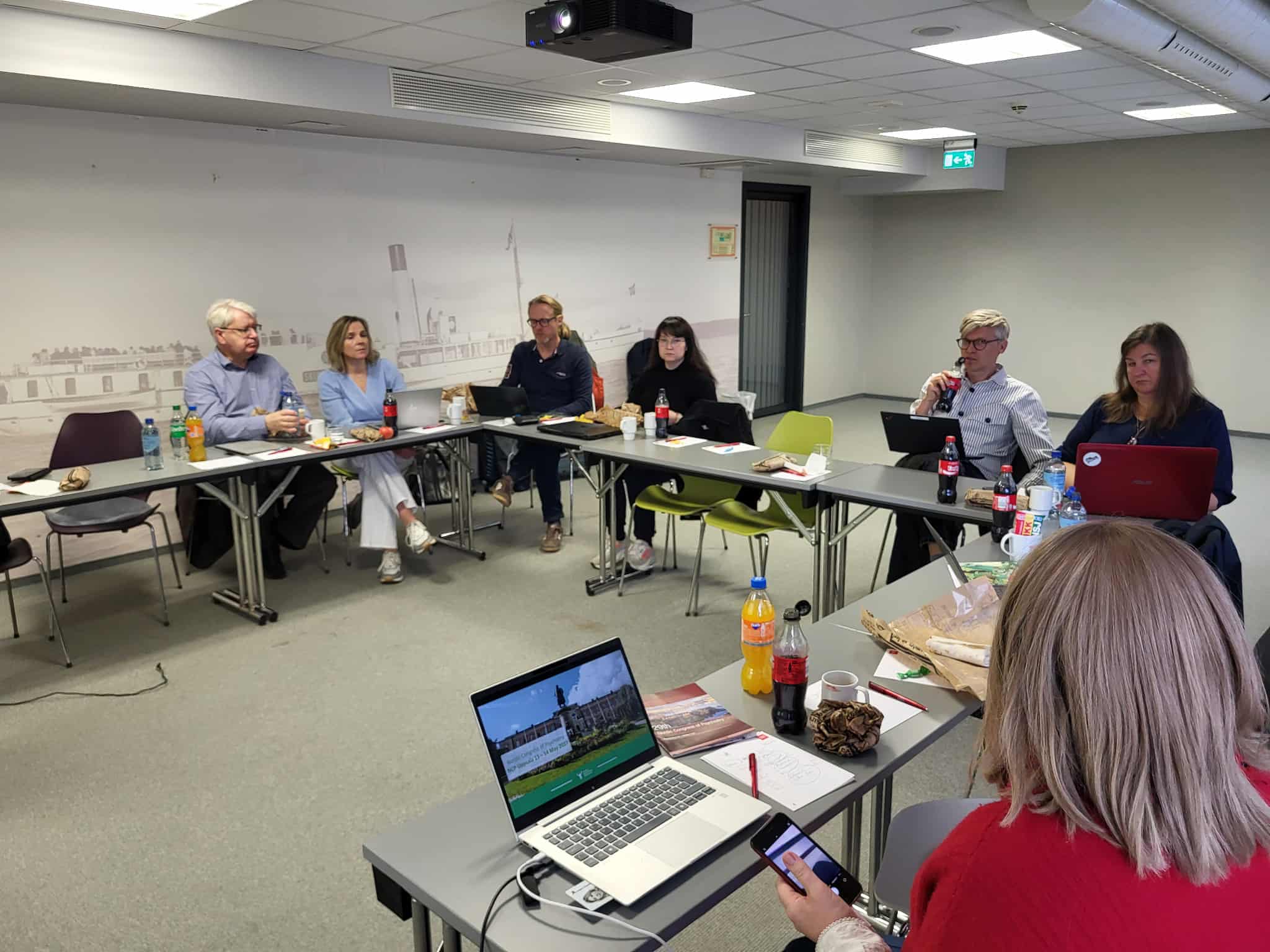 Mennesker bak bord satt i hestesko. M&oslash;terom.