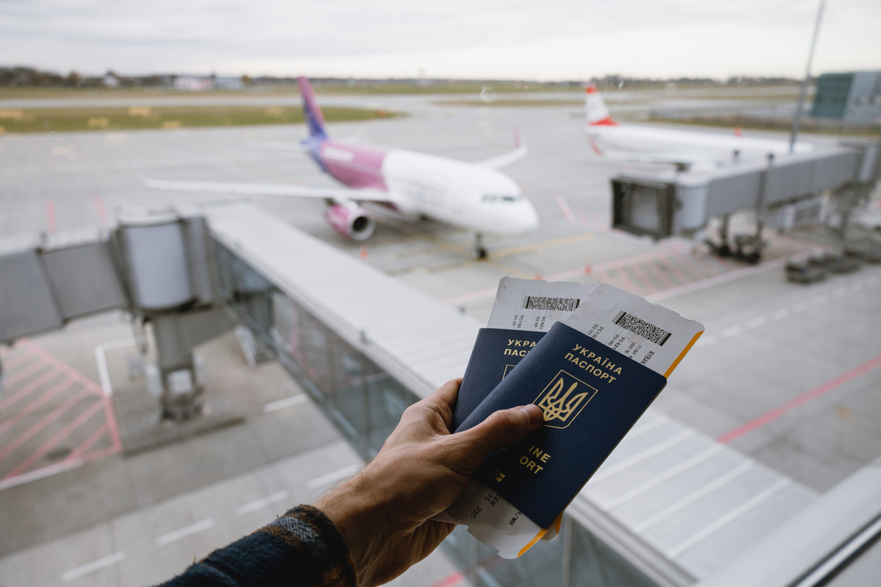 En hånd som holder to ukrainske plass med en flyplass i bakgrunnen. Foto: Istockphoto.com