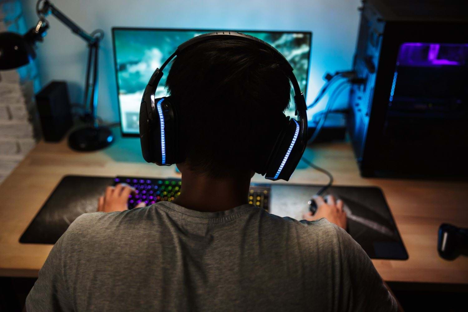 Ung mann sittende med ryggen til foran en datamaskin og spiller et spill. Foto: Colourbox.com