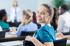 Kvinnelig medisinstudent snur seg mot kamera og smiler under en forelesning. Foto: Istockphoto.com
