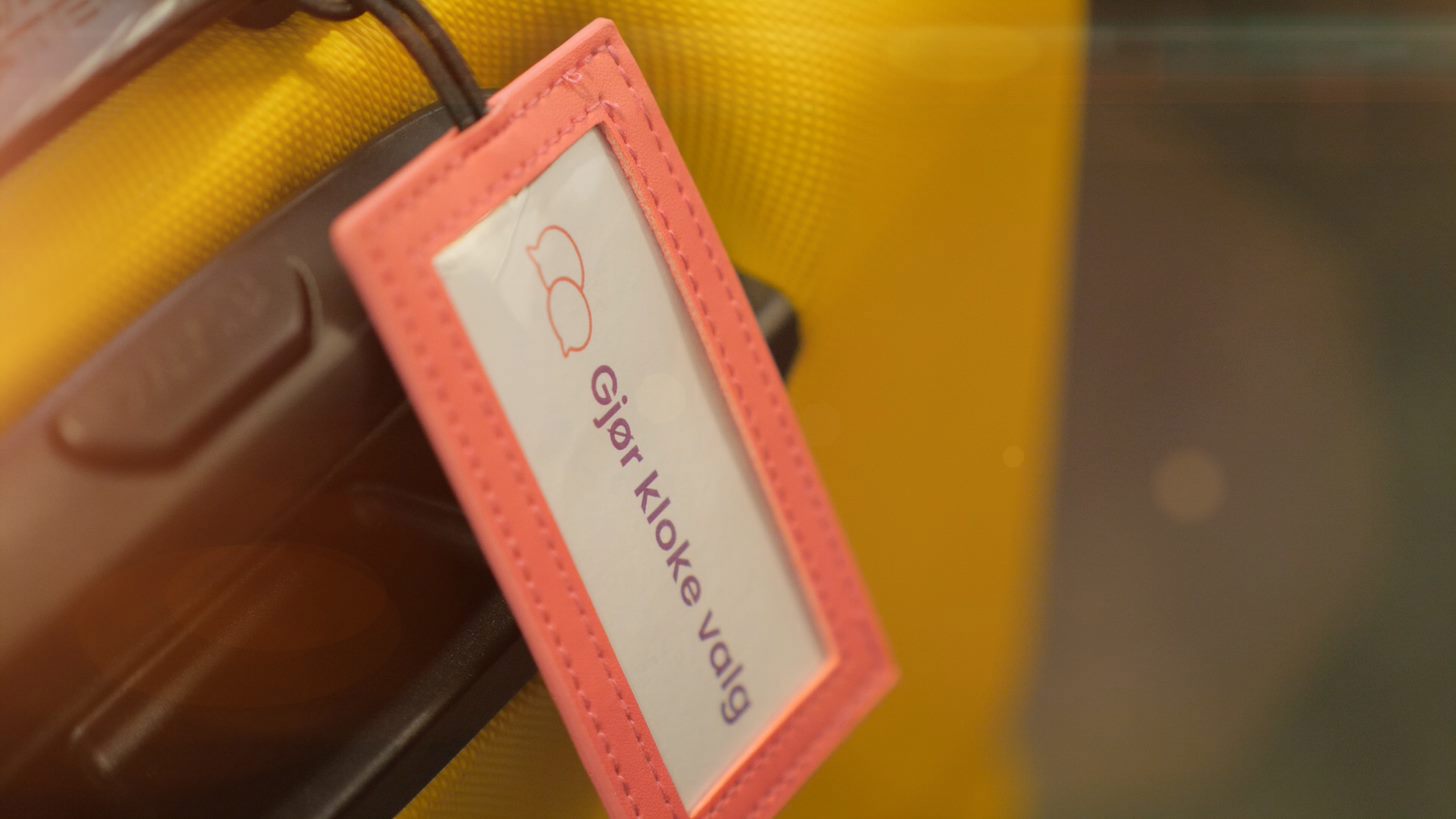 Gul koffert med navnelapp der det står "gjør kloke valg"